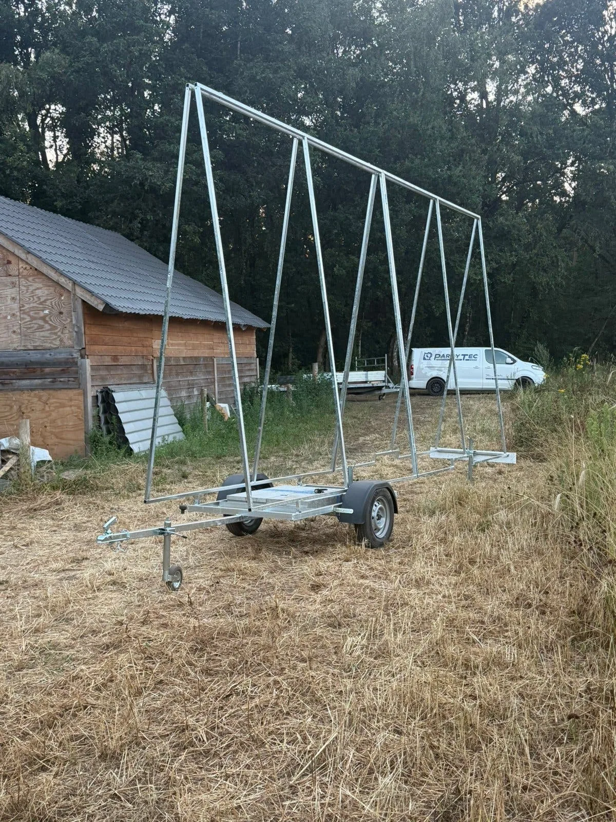 Reclameaanhangwagen schuin van voren op het erf, met een bedrijfsbus op de achtergrond